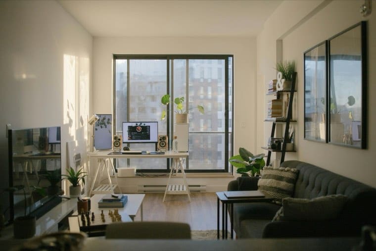 A sunlit home office with a desk, computer, and sofa in a living room