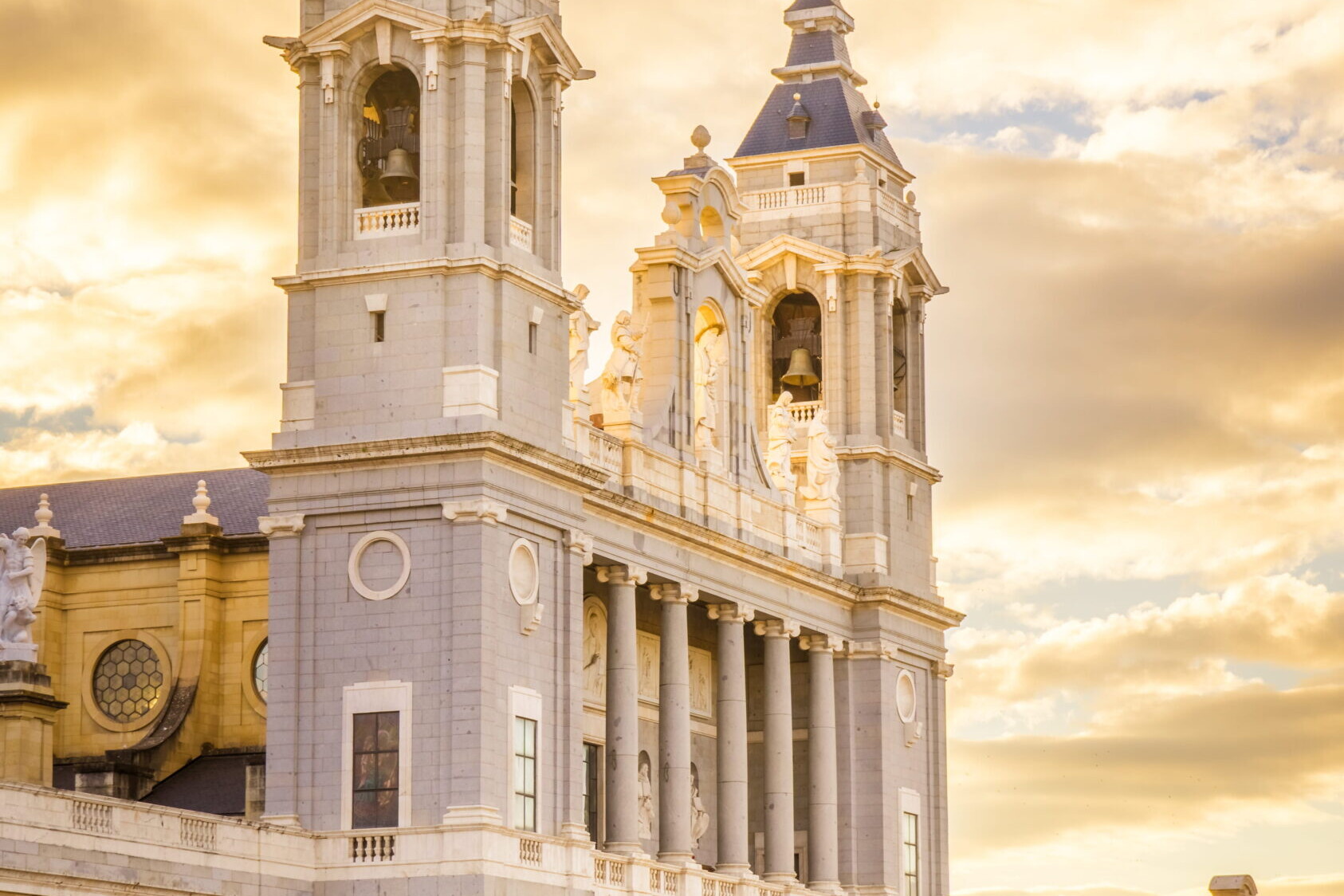 Cath&eacute;drale de Madrid avec ses deux tours et sa fa&ccedil;ade monumentale &eacute;clair&eacute;e par un ciel dor&eacute; au coucher du soleil.
