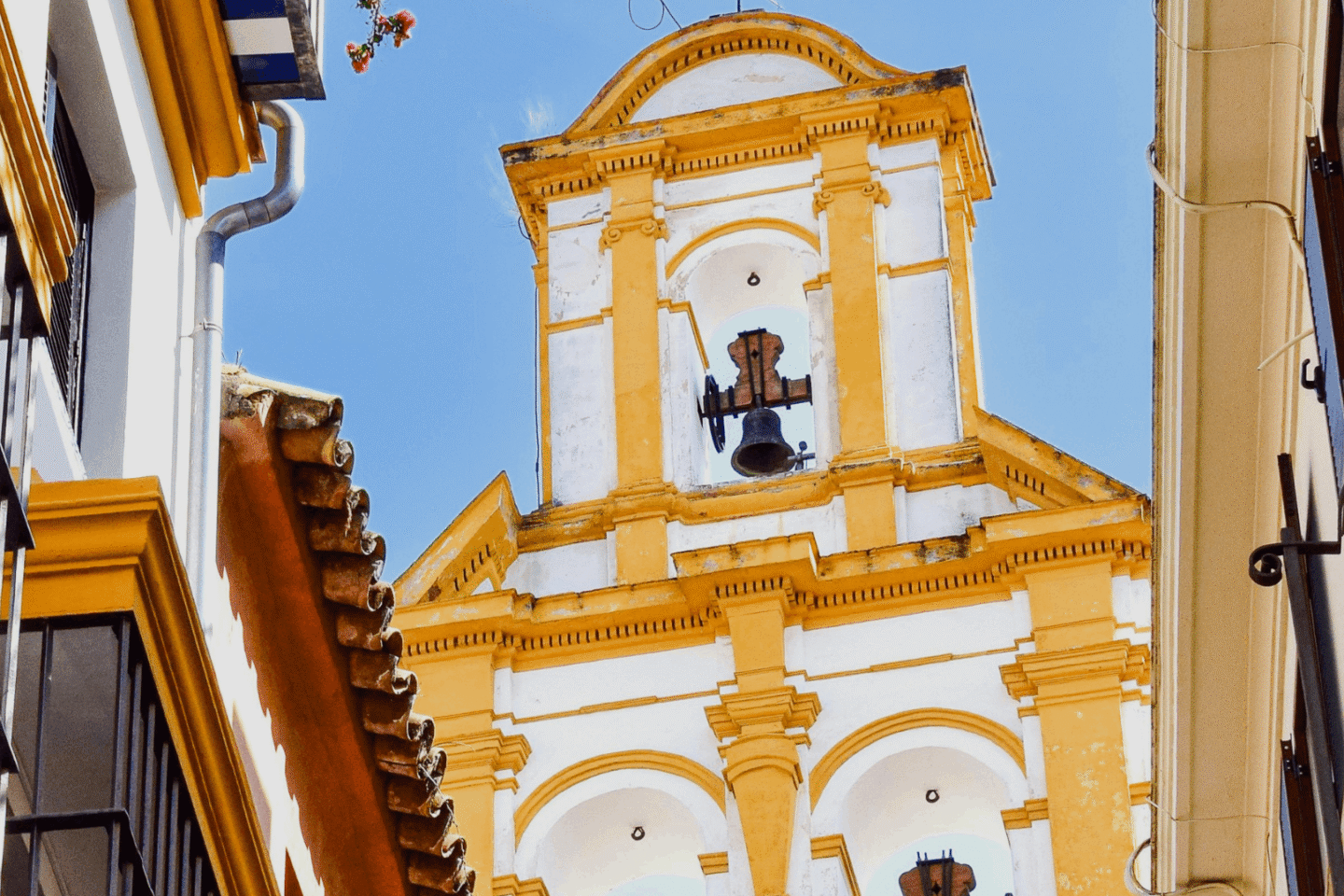 Clocher d&rsquo;&eacute;glise &agrave; S&eacute;ville avec fa&ccedil;ades blanches et jaunes, cloches apparentes et ruelle &eacute;troite typique