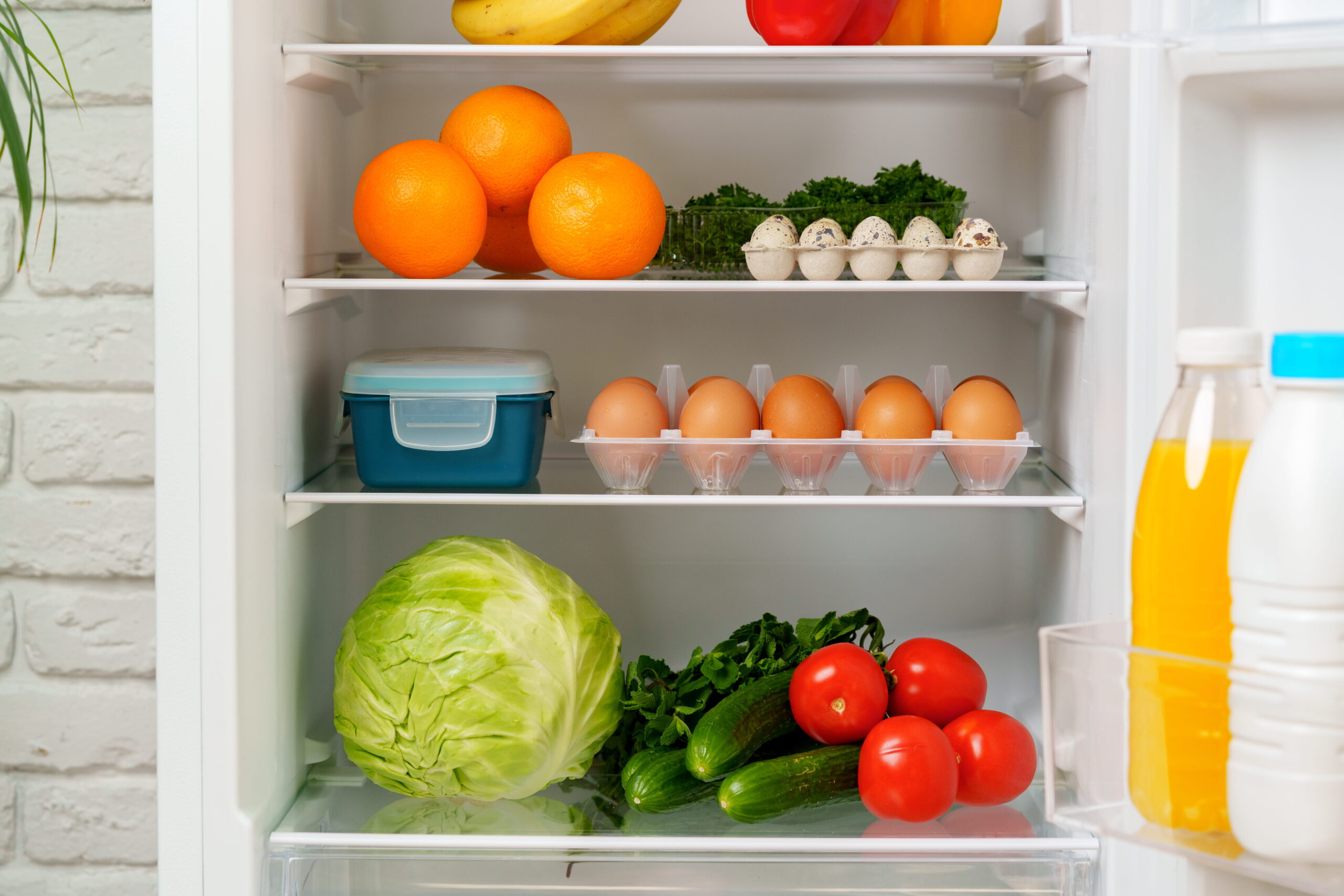 R&eacute;frig&eacute;rateur ouvert contenant des oranges, des &oelig;ufs, du chou, des tomates, des concombres et du jus d&rsquo;orange, illustrant un frigo rempli avant l&rsquo;arriv&eacute;e dans un logement Airbnb.