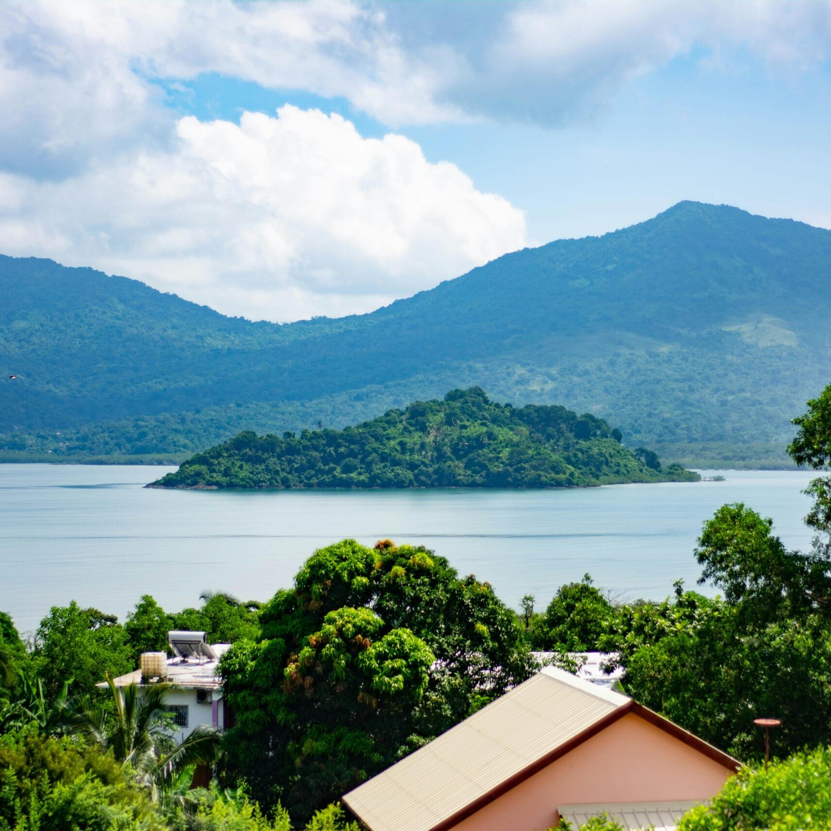 Paysage de Mayotte avec lagon, petite île verdoyante, montagnes en arrière-plan et habitations au premier plan