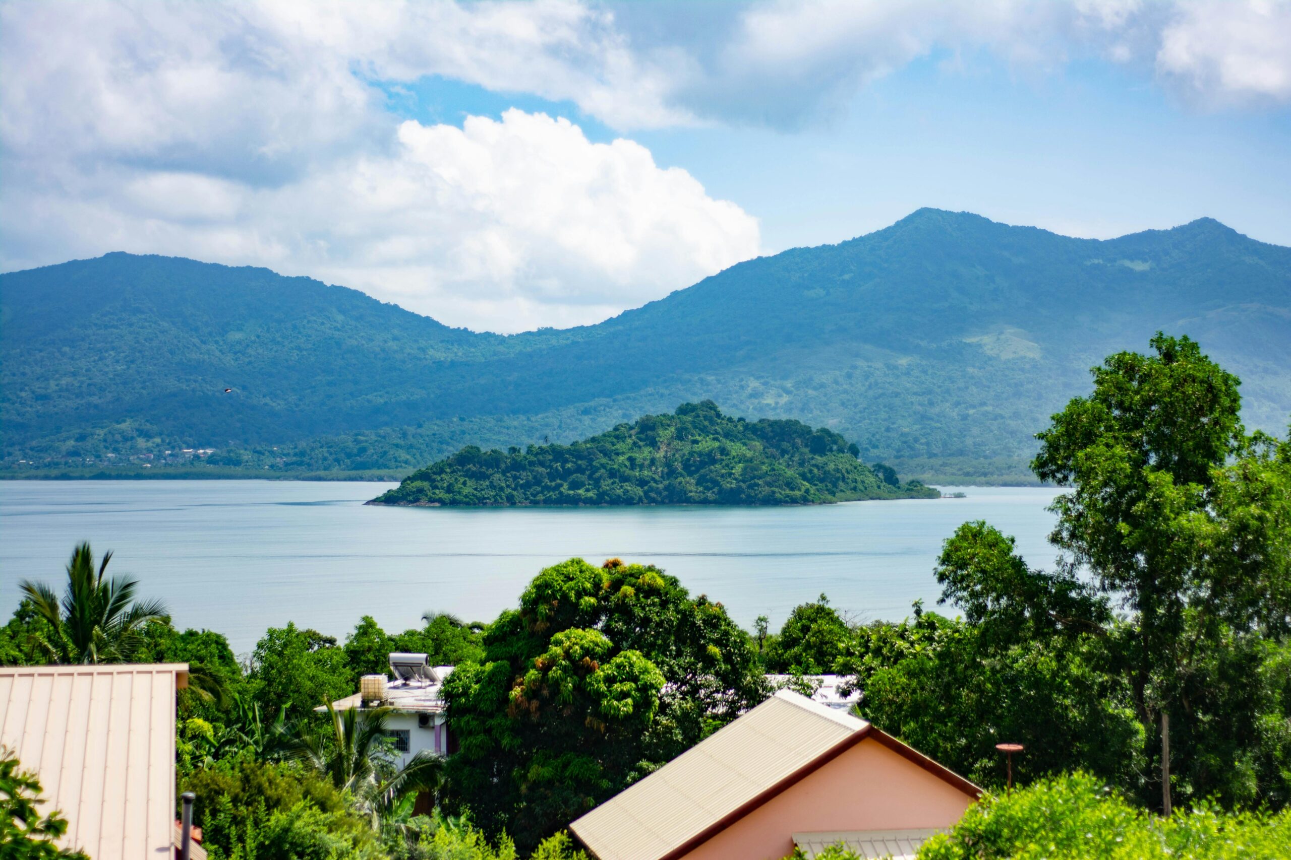 Paysage de Mayotte avec lagon, petite île verdoyante, montagnes en arrière-plan et habitations au premier plan