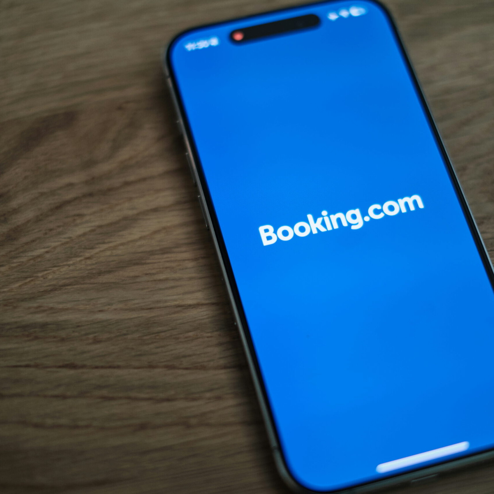 Smartphone affichant l’application Booking.com sur un écran bleu posé sur une table en bois