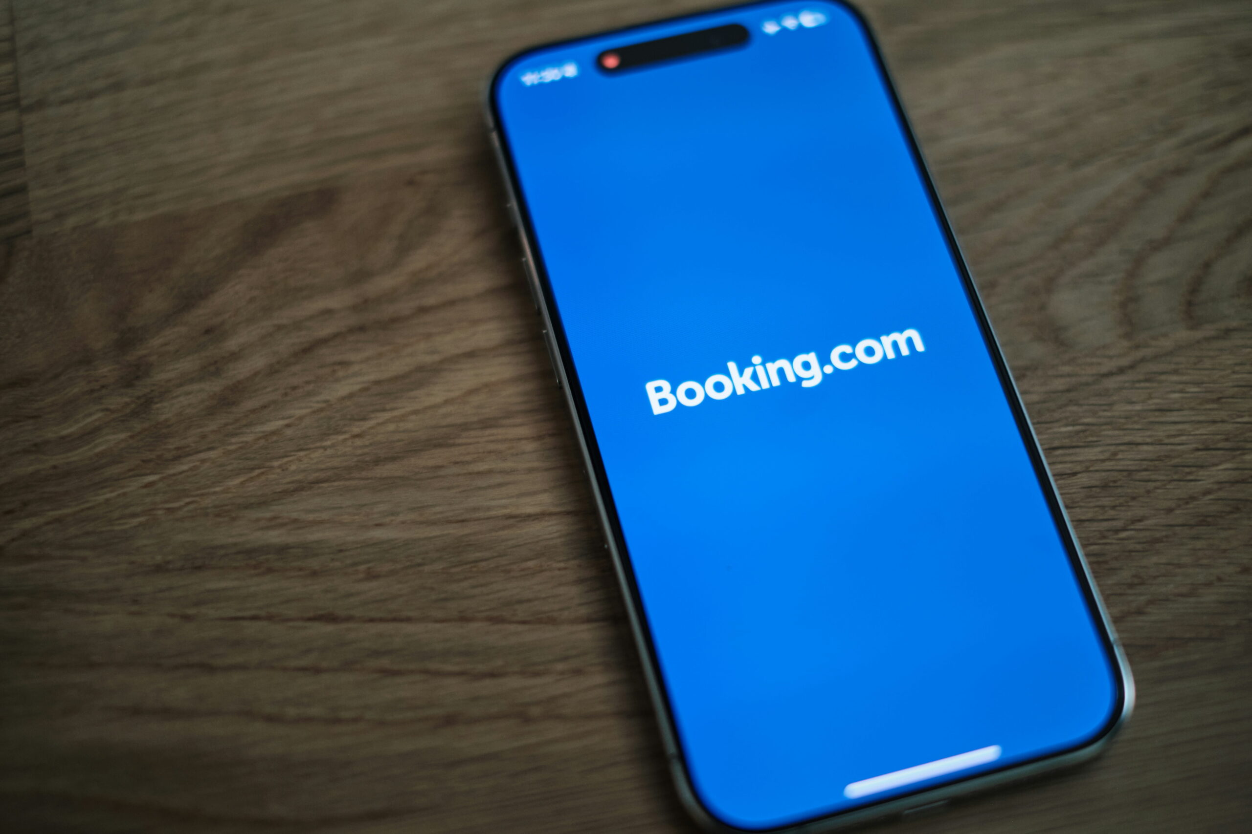 Smartphone affichant l’application Booking.com sur un écran bleu posé sur une table en bois