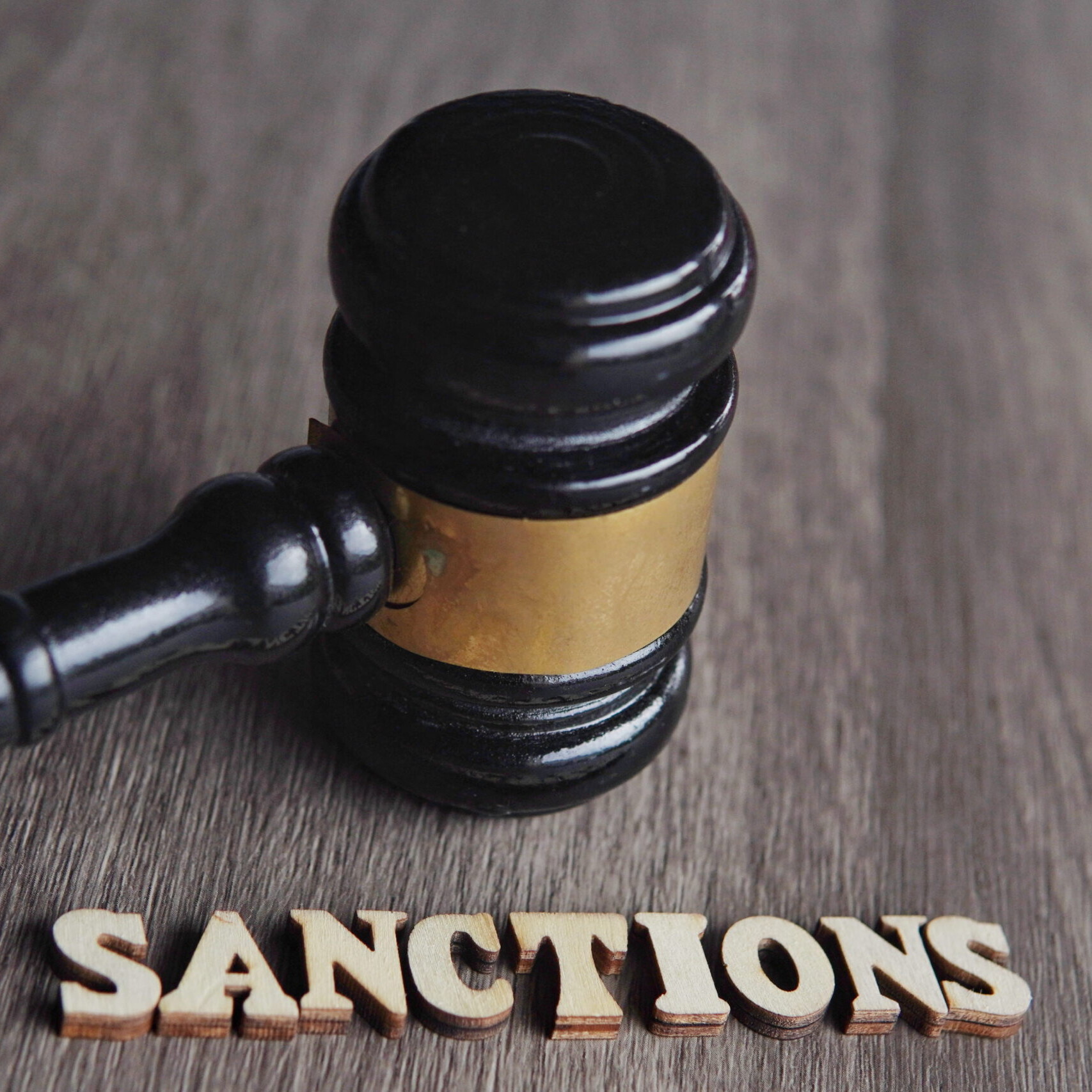 Marteau de juge posé sur une table avec le mot sanctions écrit en bois, symbolisant les sanctions juridiques