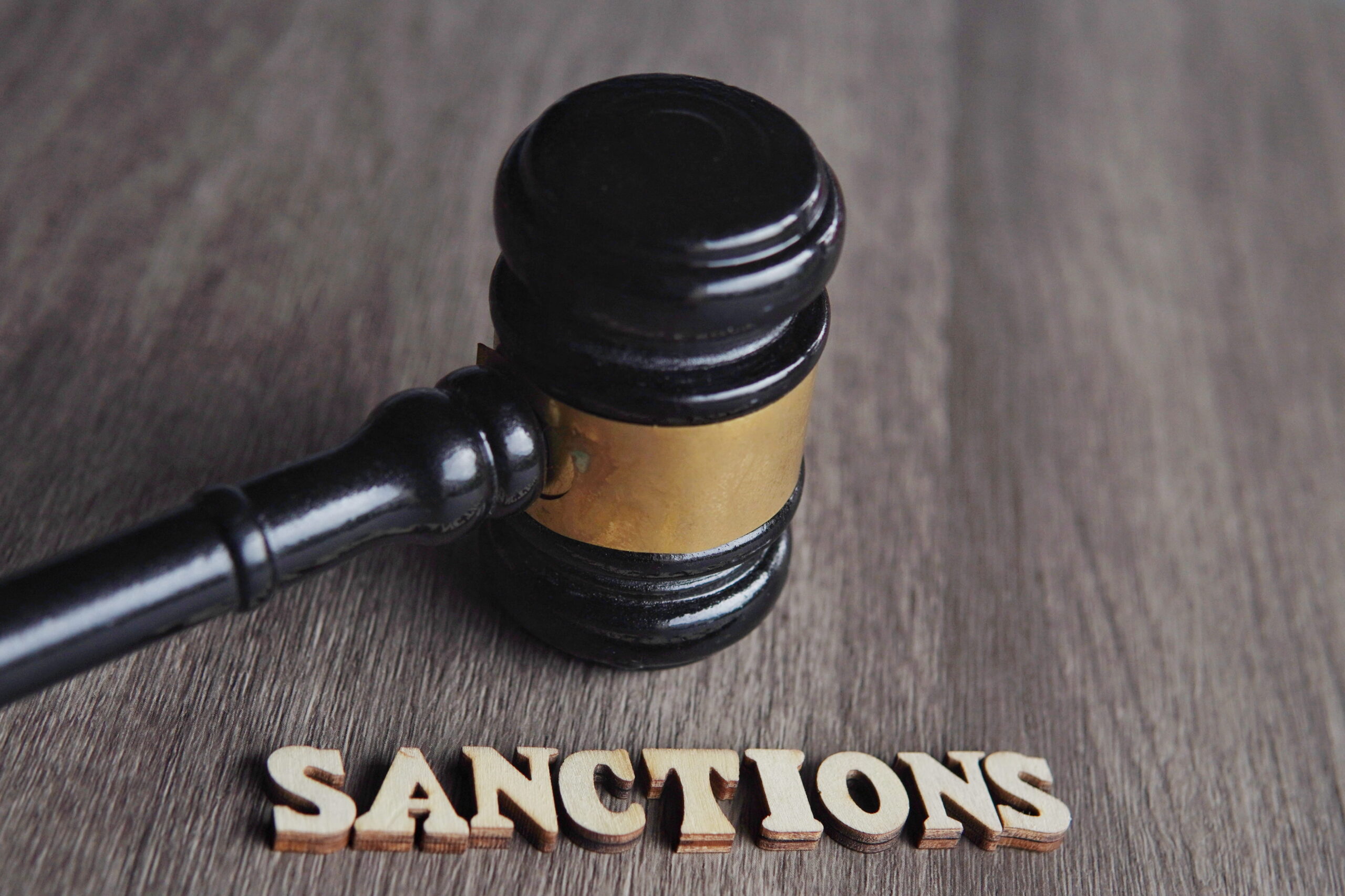 Marteau de juge posé sur une table avec le mot sanctions écrit en bois, symbolisant les sanctions juridiques