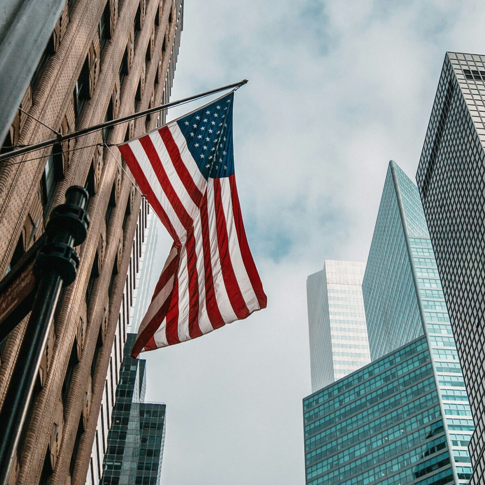Drapeau des États-Unis flottant entre des gratte-ciel à New York, illustrant le tourisme et les voyages aux États-Unis.