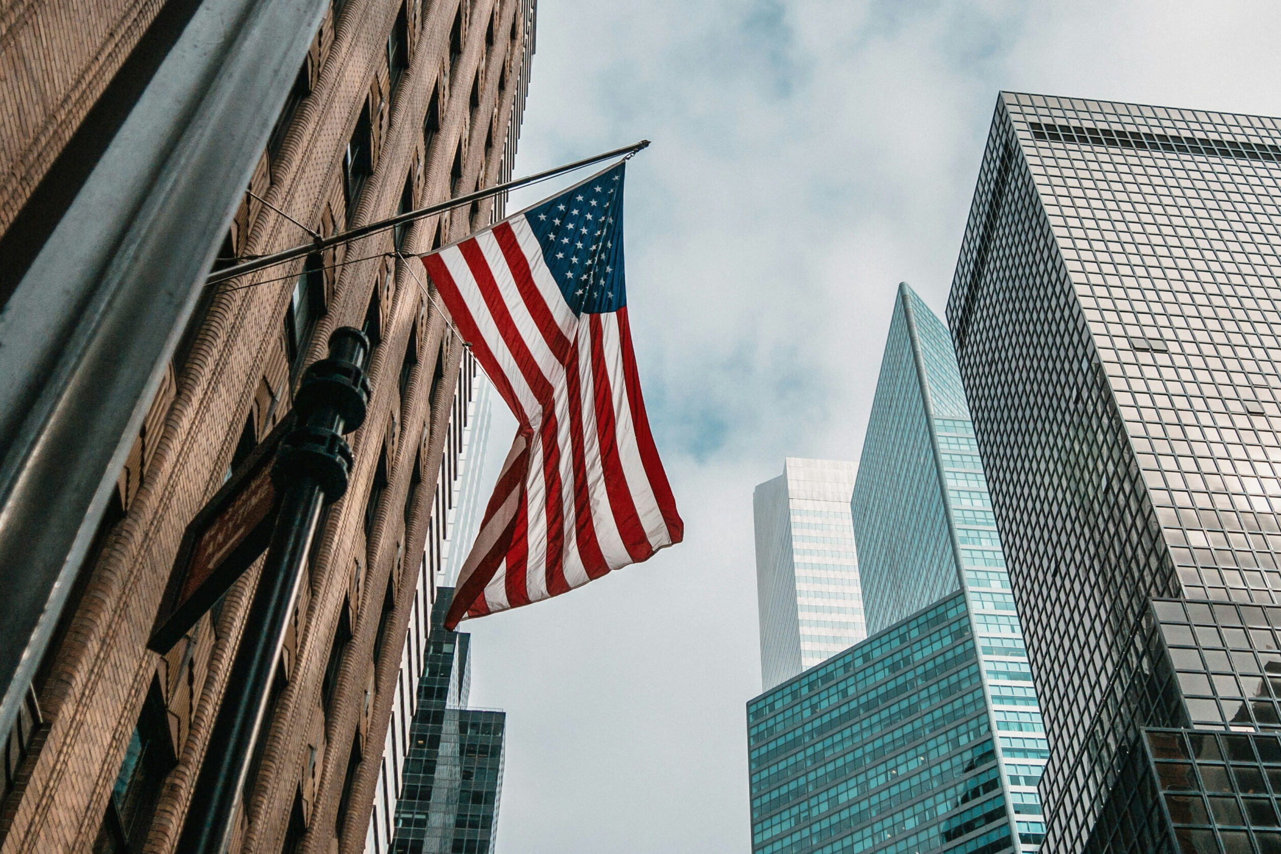 Drapeau des États-Unis flottant entre des gratte-ciel à New York, illustrant le tourisme et les voyages aux États-Unis.